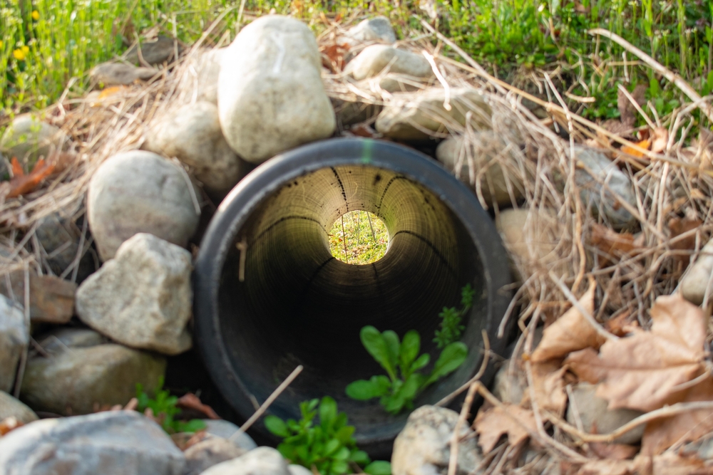 Looking Through a French Drain With a Black Pipe and Large Rocks Surrounding It